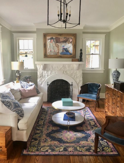 Vintage Modern Home Decor Ideas: 15 Ways to Mix Old and New "A cozy and elegant living room highlighting Vintage Modern Home Decor Ideas, featuring a white stone fireplace, a light-colored sofa with patterned throw pillows, a two-tier round coffee table, a classic patterned area rug, and a rustic wooden dresser."