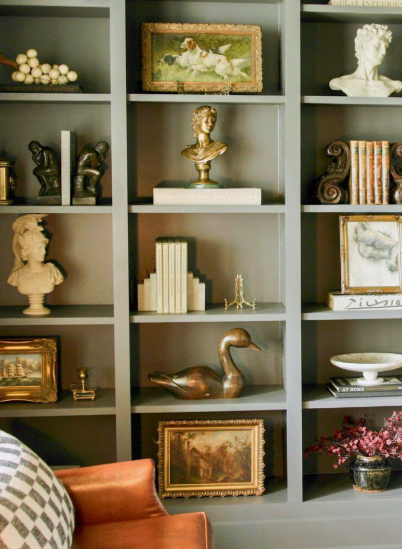 Vintage Modern Home Decor Ideas: 15 Ways to Mix Old and New "A styled gray bookshelf showcasing Vintage Modern Home Decor Ideas, featuring an array of antique brass animal figurines, classical busts, framed vintage paintings, decorative books, and sculptural objects."