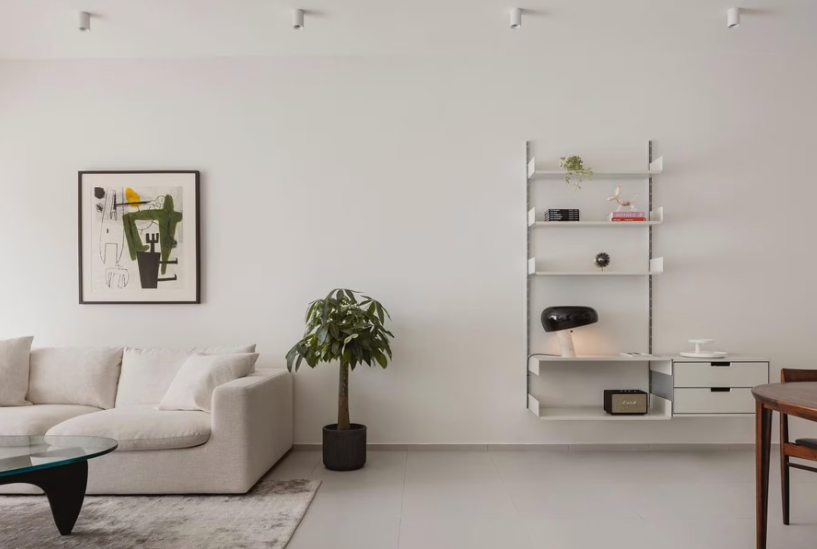Vintage Modern Home Decor Ideas: 15 Ways to Mix Old and New "A minimalist and bright living space highlighting Vintage Modern Home Decor Ideas, featuring a sleek white sectional sofa, abstract modern wall art, a potted houseplant, a modular wall shelving unit, and a glass-top coffee table."