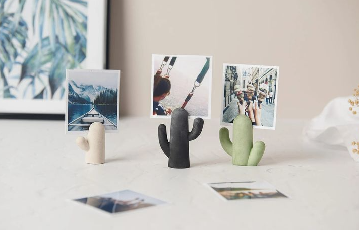 Three cute cactus-shaped air dry clay crafts functioning as photo holders on a white table, each holding a small polaroid picture
