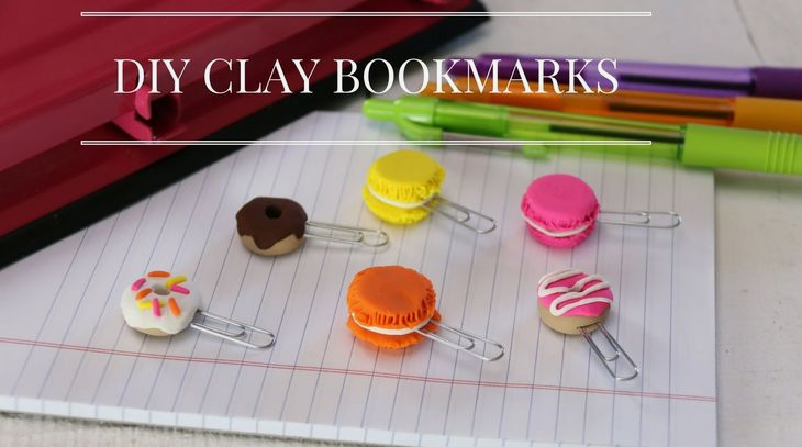 A close-up of colorful air dry clay crafts functioning as DIY bookmarks attached to paper clips on a lined notebook, featuring miniature donuts and macarons.