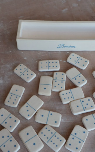 A set of handmade white dominoes with blue dots laid out next to a custom storage box, illustrating fun air dry clay ideas for custom board games.
