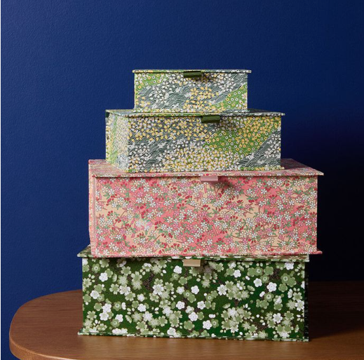 A stack of four decorative storage boxes wrapped in floral and patterned chiyogami paper against a dark blue background.