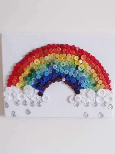 30 Creative DIY Button Crafts to Turn Spare Buttons Into Beautiful Decor A colorful canvas wall art piece displaying a rainbow arched across the canvas, made of multicolored buttons with white button clouds and dangling crystal teardrops representing raindrops, highlighting DIY button crafts.