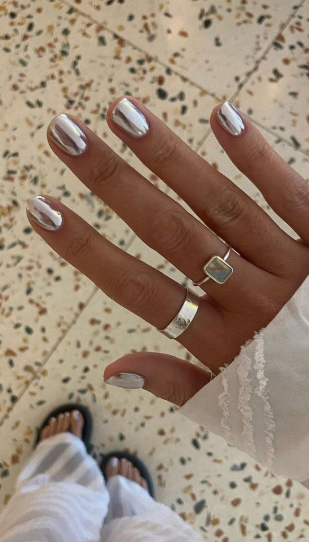Short nails with high-shine metallic silver chrome finish, accessorized with matching silver rings.