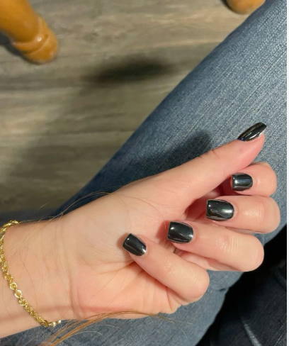 Short black chrome nails with a highly reflective metallic sheen, paired with a gold bracelet and blue jeans.