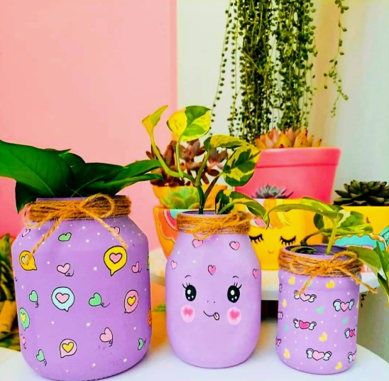 20 Recycled Household Item Crafts for a Creative Home A collection of recycled household item crafts featuring three purple painted glass jars used as plant pots, decorated with playful doodles, twine bows, and holding small green plants against a colorful backdrop.