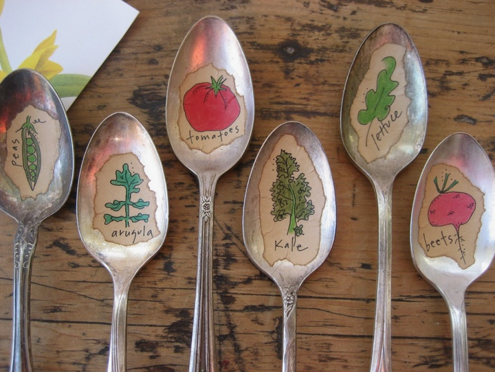 20 Recycled Household Item Crafts for a Creative Home A group of vintage spoons repurposed as recycled household item crafts for garden markers, featuring hand-drawn illustrations and labels for peas, arugula, tomatoes, kale, lettuce, and beets placed on a wooden surface.