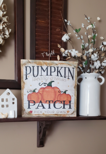 20 Recycled Household Item Crafts for a Creative Home A recycled household item craft featuring a farmhouse-style autumn sign with a "Pumpkin Patch" graphic, displayed on a wooden shelf alongside a white ceramic house figurine and a white vase filled with cotton stems.