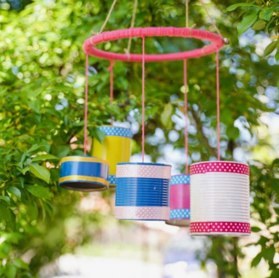 20 Recycled Household Item Crafts for a Creative Home A hanging wind chime created as a recycled household item craft from colorful tin cans suspended by pink strings from a wrapped circular hoop hanging among green foliage.
