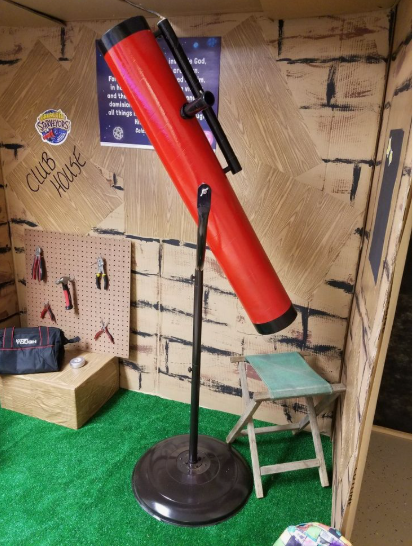 20 Recycled Household Item Crafts for a Creative Home A recycled household item craft featuring a large telescope prop built from a painted cardboard tube mounted on a metal stand inside a cardboard clubhouse set.