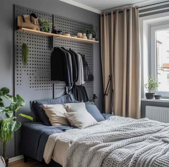 Small bedroom idea with no closet featuring a large dark gray pegboard wall above the bed used for hanging clothes, displaying accessories, and holding wall-mounted wooden shelves.
