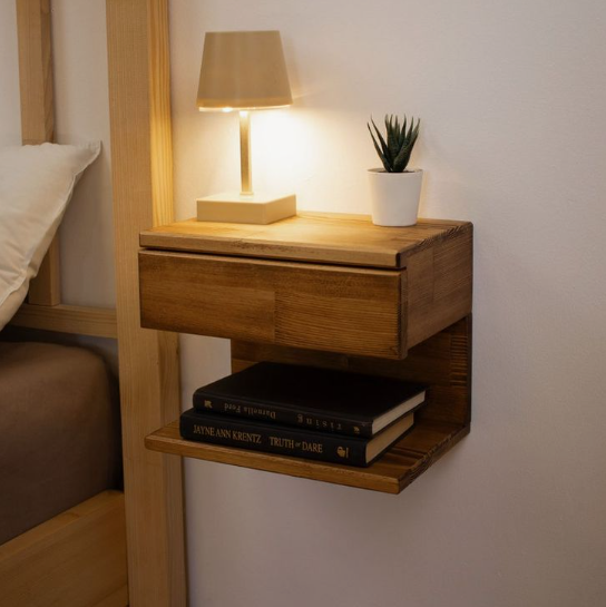 Small bedroom idea with no closet featuring a wall-mounted floating wooden nightstand with a storage drawer, lower shelf holding stacked books, a compact table lamp, and a small potted plant.