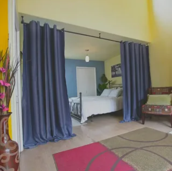 Small bedroom idea with no closet featuring a room divider setup with long dark blue curtains on an overhead rod creating a private, makeshift enclosure for a bed inside the alcove