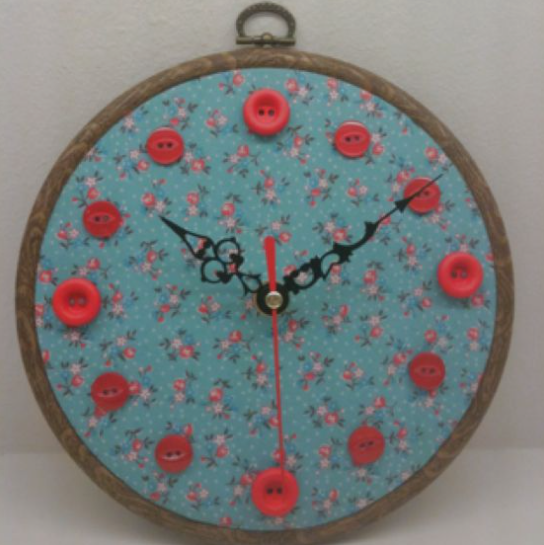 30 Creative DIY Button Crafts to Turn Spare Buttons Into Beautiful Decor A round wall clock set inside an embroidery hoop, featuring a blue floral fabric face with red buttons marking the hours and black clock hands, highlighting DIY button crafts.