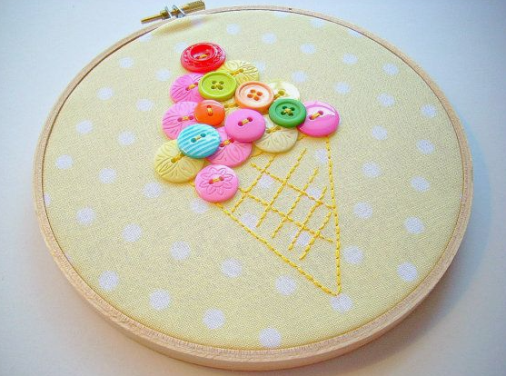 30 Creative DIY Button Crafts to Turn Spare Buttons Into Beautiful Decor A framed embroidery hoop art piece featuring a pastel fabric background with a stitched waffle cone and a colorful mound of buttons forming an ice cream scoop, highlighting DIY button crafts.