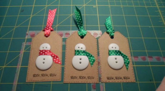 30 Creative DIY Button Crafts to Turn Spare Buttons Into Beautiful Decor A set of three brown kraft paper holiday gift tags featuring cute snowmen made from stacked white buttons wearing polka-dot ribbon scarves, topped with matching hanging ribbons, highlighting DIY button crafts.