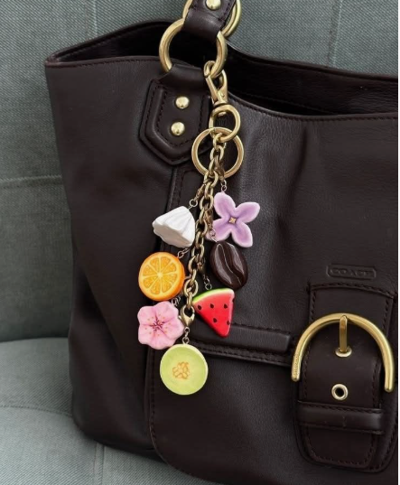 DIY clay bag charms attached to a dark brown leather purse, featuring colorful handmade charms including flowers, a slice of orange, a watermelon wedge, and coffee beans.