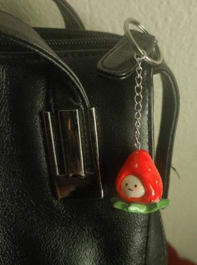 DIY clay bag charms featuring a cute handmade strawberry-themed character attached to a black leather bag.