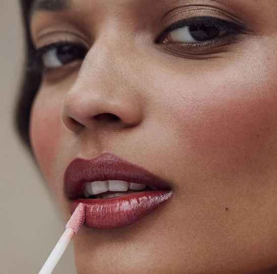 Close-up of a model applying lip gloss to deep berry lips as part of Fall 2026 Beauty Trends.