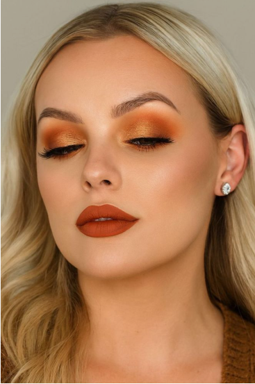 Blonde model featuring warm autumn orange eyeshadow and a matching matte lip that embodies Fall 2026 Beauty Trends.