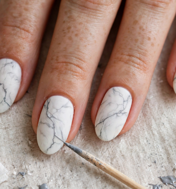 White and grey marble nail art for beginners being painted with a fine detail brush on oval nails.   