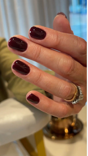 Close-up of glossy deep burgundy nails featuring delicate line art details that capture Fall 2026 Beauty Trends.