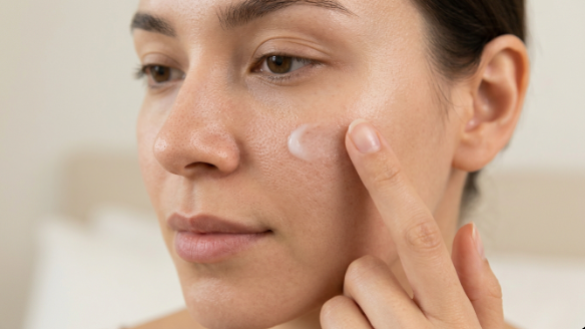 A woman applying hydrating facial cream onto her cheek as pre-makeup skin prep to resolve why does my makeup look dry.