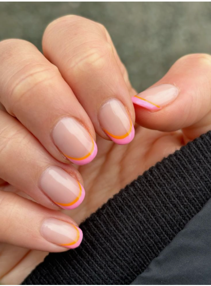 35 Short Nail Designs That Make Your Fingers Look Longer A close-up of short, rounded nails featuring a double-line French tip in vibrant pink and orange on a sheer base, serving as one of the short nail designs that make your fingers look longer.