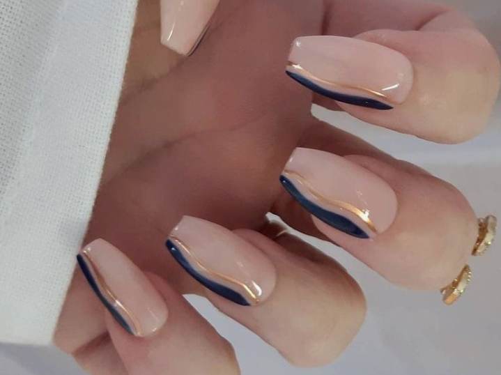 35 Short Nail Designs That Make Your Fingers Look Longer A close-up of short, square nails featuring a neutral base with abstract dark blue and gold curved lines, demonstrating one of the short nail designs that make your fingers look longer.