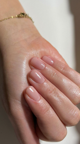 35 Short Nail Designs That Make Your Fingers Look Longer A close-up of short, neatly manicured square nails in a glossy neutral nude shade, creating a clean look that serves as one of the short nail designs that make your fingers look longer.