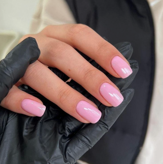 35 Short Nail Designs That Make Your Fingers Look Longer A close-up of short, square nails painted in a glossy pastel pink, providing a clean style that serves as one of the short nail designs that make your fingers look longer.