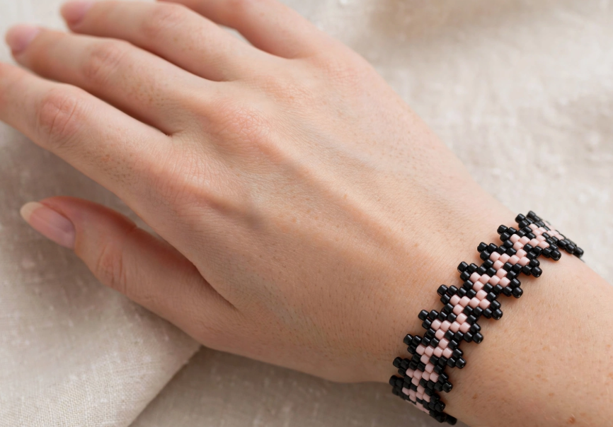 Hand wearing a DIY beaded zigzag bracelet in black and soft pink, an elegant project for craft ideas for adults.   