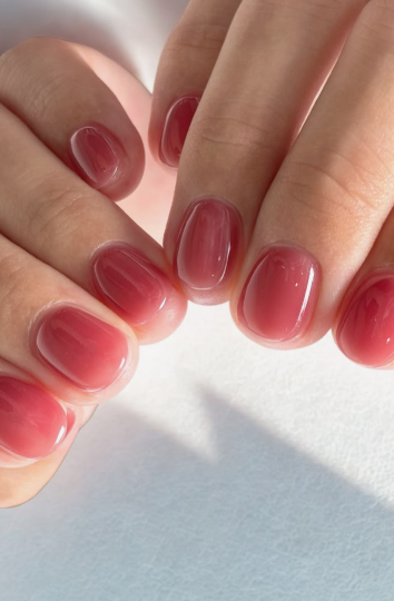 35 Short Nail Designs That Make Your Fingers Look Longer A close-up of short, rounded nails finished in a glossy, translucent berry-pink syrup gel, creating a clean look that serves as one of the short nail designs that make your fingers look longer.