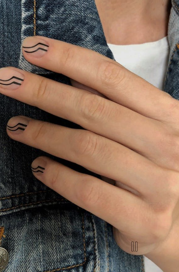 35 Short Nail Designs That Make Your Fingers Look Longer A close-up of short, rounded nails featuring minimalist black wavy lines on a neutral nude base against a denim jacket, representing one of the short nail designs that make your fingers look longer.