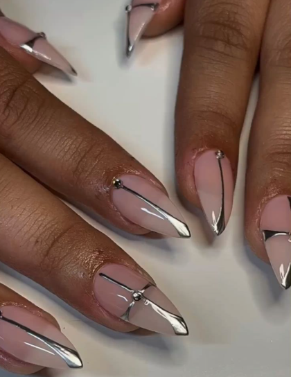35 Short Nail Designs That Make Your Fingers Look Longer A close-up of long, stiletto-shaped nails with metallic silver chrome geometric accents and piercing rings on a nude base, representing an elongated variation compared to short nail designs that make your fingers look longer.