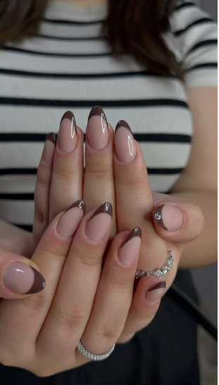 35 Short Nail Designs That Make Your Fingers Look Longer A close-up of short, almond-shaped nails featuring a rich dark brown French tip on a sheer neutral base, serving as one of the short nail designs that make your fingers look longer.