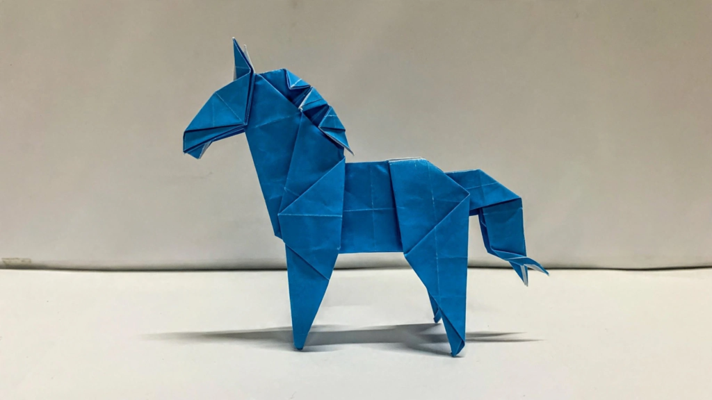 A standing origami horse folded from vibrant blue paper against a white background, showcasing analog crafts to do instead of scrolling.   
