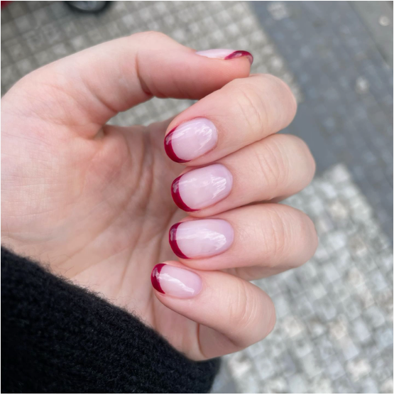 35 Short Nail Designs That Make Your Fingers Look Longer A close-up of short, rounded nails showcasing deep burgundy red French tips on a sheer neutral base, serving as one of the short nail designs that make your fingers look longer.