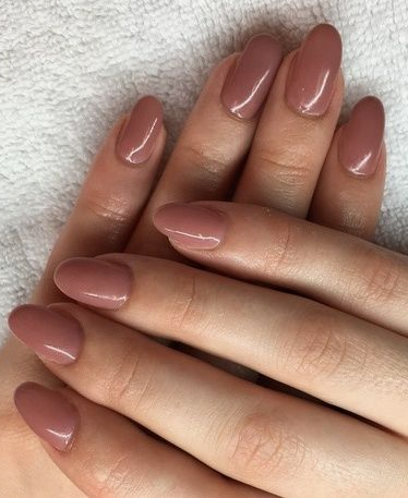 35 Short Nail Designs That Make Your Fingers Look Longer A close-up of short, oval nails finished in a glossy warm dusty rose polish, serving as one of the short nail designs that make your fingers look longer.