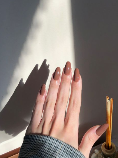 35 Short Nail Designs That Make Your Fingers Look Longer A close-up of short, oval-shaped nails finished in a glossy rich milk chocolate brown polish, serving as one of the short nail designs that make your fingers look longer.