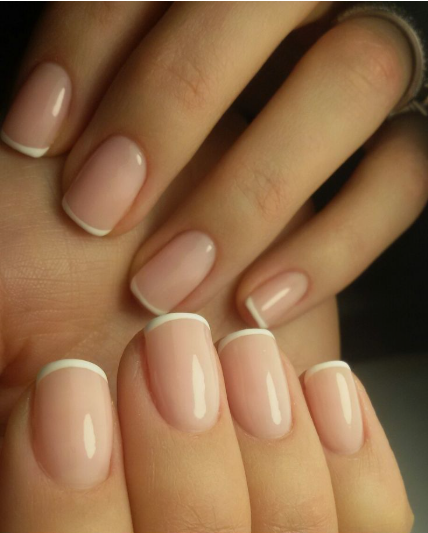 35 Short Nail Designs That Make Your Fingers Look Longer A close-up of short, squared-oval nails featuring classic white French tips on a sheer milky nude base, serving as one of the short nail designs that make your fingers look longer.