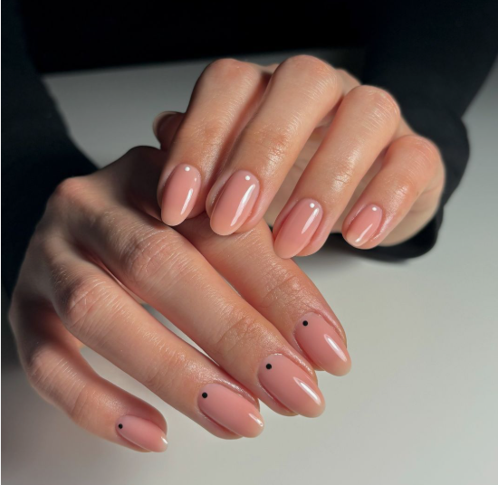 35 Short Nail Designs That Make Your Fingers Look Longer A close-up of short, oval nails finished in a glossy neutral pink polish with a tiny minimalist black dot near the cuticle on each nail, serving as one of the short nail designs that make your fingers look longer.