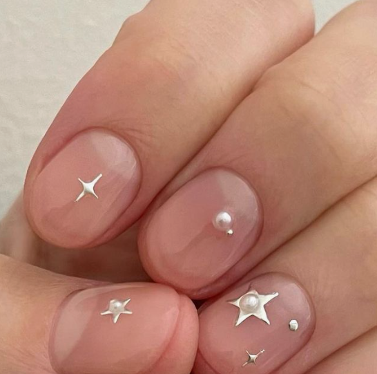 35 Short Nail Designs That Make Your Fingers Look Longer A close-up of short, rounded nails showcasing dainty silver star studs and tiny pearls on a sheer nude base, serving as one of the short nail designs that make your fingers look longer.