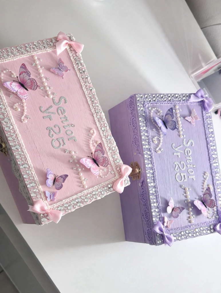 Handmade pink and purple senior keepsake memory boxes with butterfly and pearl accents, showcasing craft ideas for teens[cite: 26].