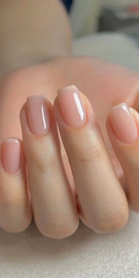 35 Short Nail Designs That Make Your Fingers Look Longer A close-up of short, square-shaped nails finished in a glossy, semi-sheer neutral pink polish, serving as one of the short nail designs that make your fingers look longer.