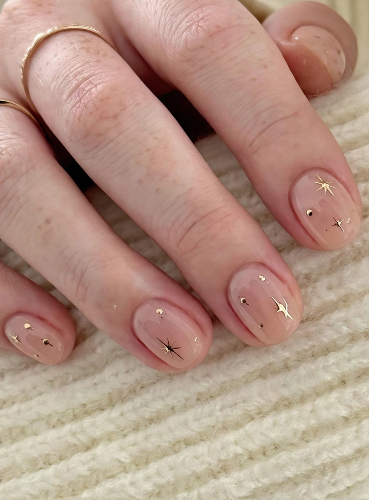 20 Minimalist Nail Designs for Short Nails Minimalist nail designs for short nails featuring glossy sheer nude polish accented with delicate gold starbursts and tiny metallic celestial studs.