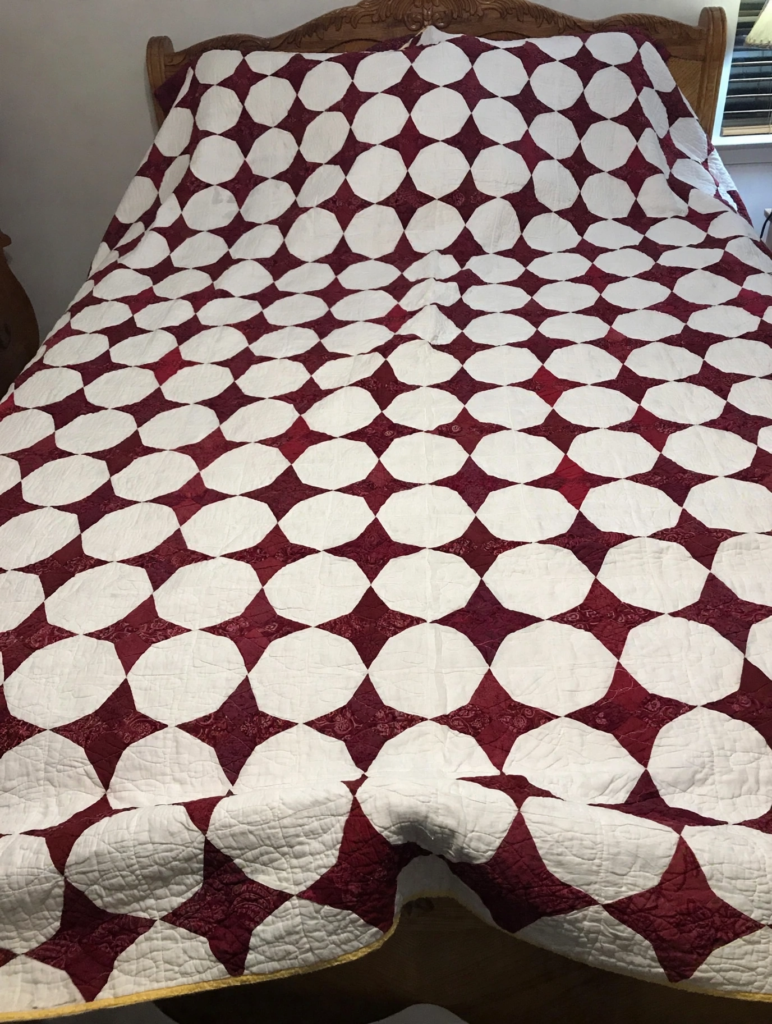 20 Nostalgic Crafts Making a Comeback in 2026 Vintage handmade patchwork quilt in a deep maroon and white geometric lattice pattern draped over a bed, inspiring nostalgic crafts 2026 bedroom decor ideas.
