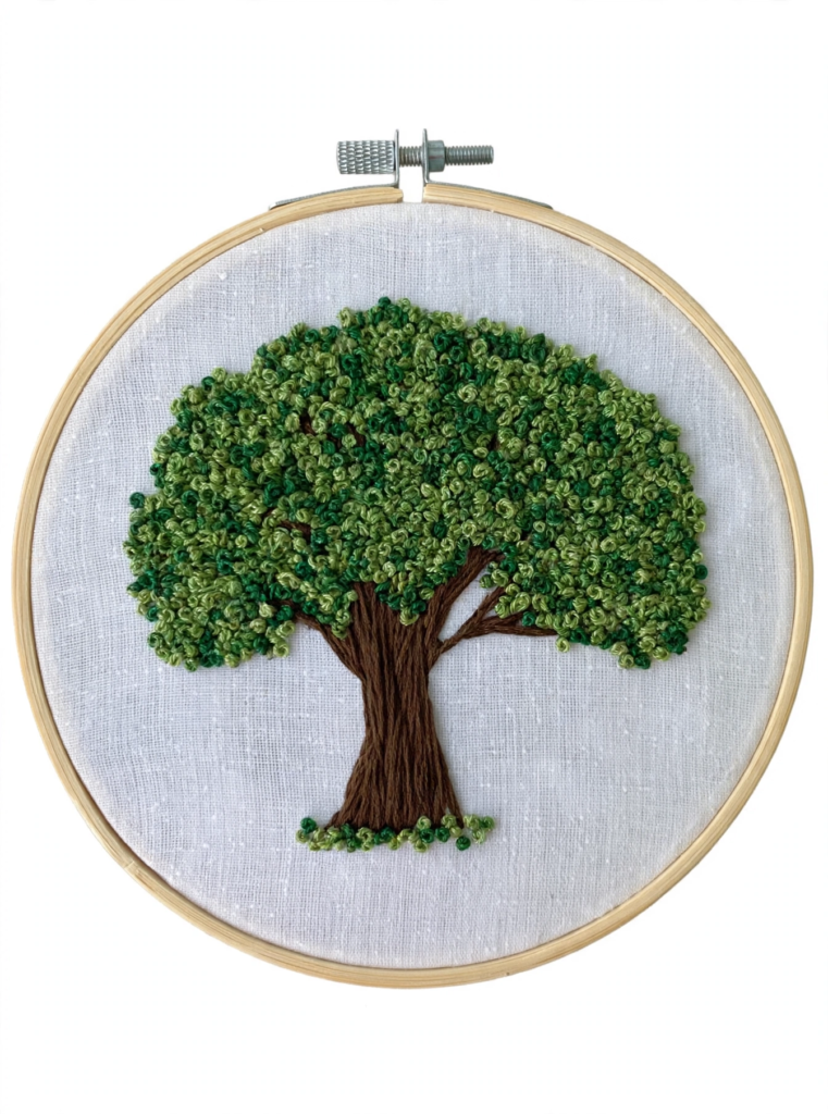 20 Nostalgic Crafts Making a Comeback in 2026 Handcrafted embroidery hoop art featuring a lush green tree with textured French knot foliage and a brown stitched trunk, representing nostalgic crafts 2026 botanical needlework ideas.