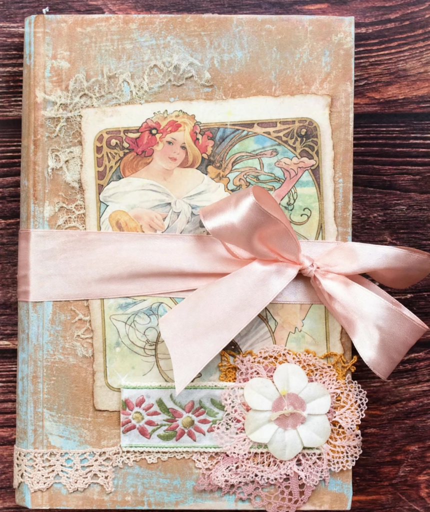 20 Nostalgic Crafts Making a Comeback in 2026 Handcrafted vintage junk journal featuring an Art Nouveau illustration, distressed textured cover, delicate lace, and a soft pink satin ribbon bow, representing nostalgic crafts 2026 paper crafting ideas.